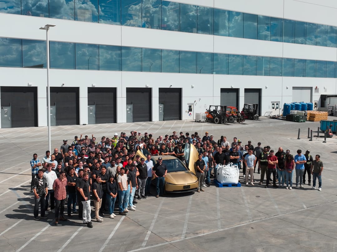 Tesla team gathered around a gold Cybercab outside a factory building