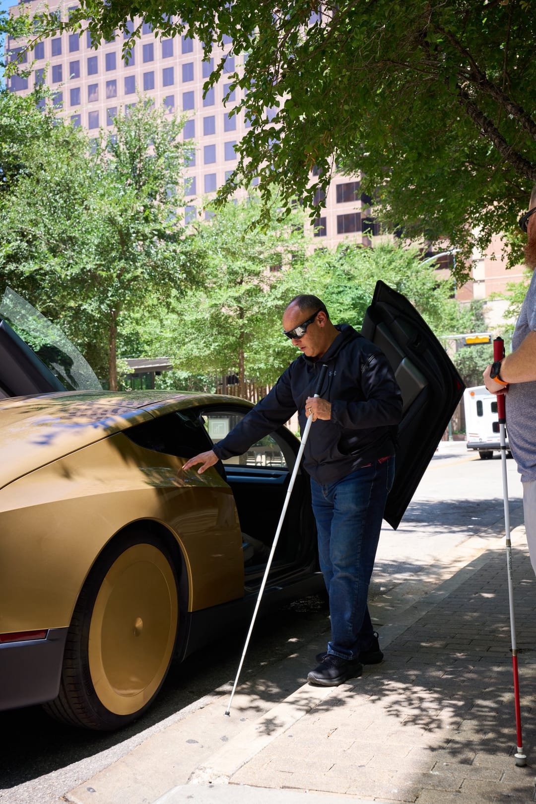 A visitor with a white cane at the open door of a gold Cybercab in Austin
