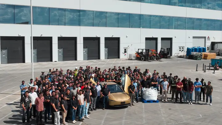 Tesla team gathered around a gold Cybercab outside a factory building