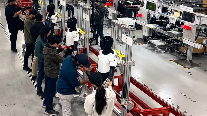 Optimus robots on a factory line, with Tesla staff working on them