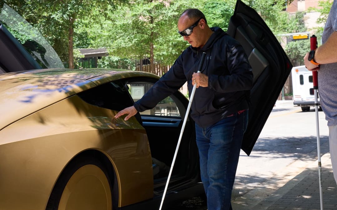 A visitor with a white cane at the open door of a gold Cybercab in Austin