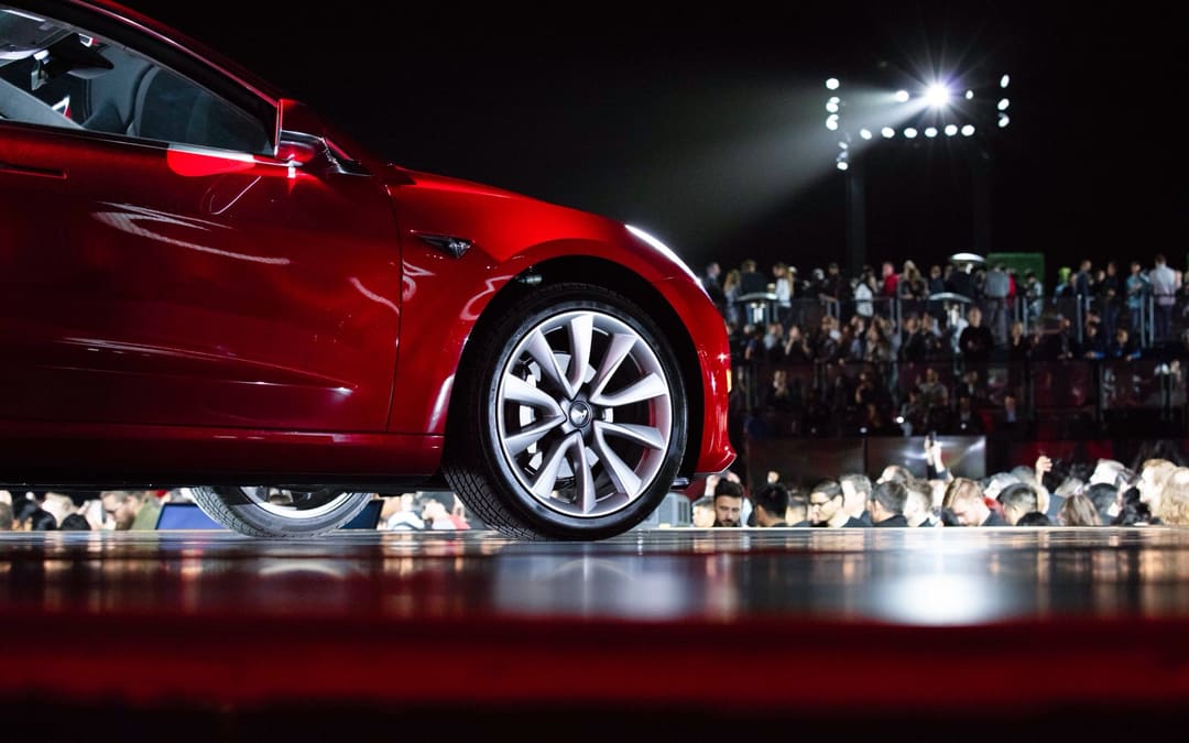 Red Model 3 under stage lights, wheel and front in close-up, from Tesla’s “10 years of Model 3” post