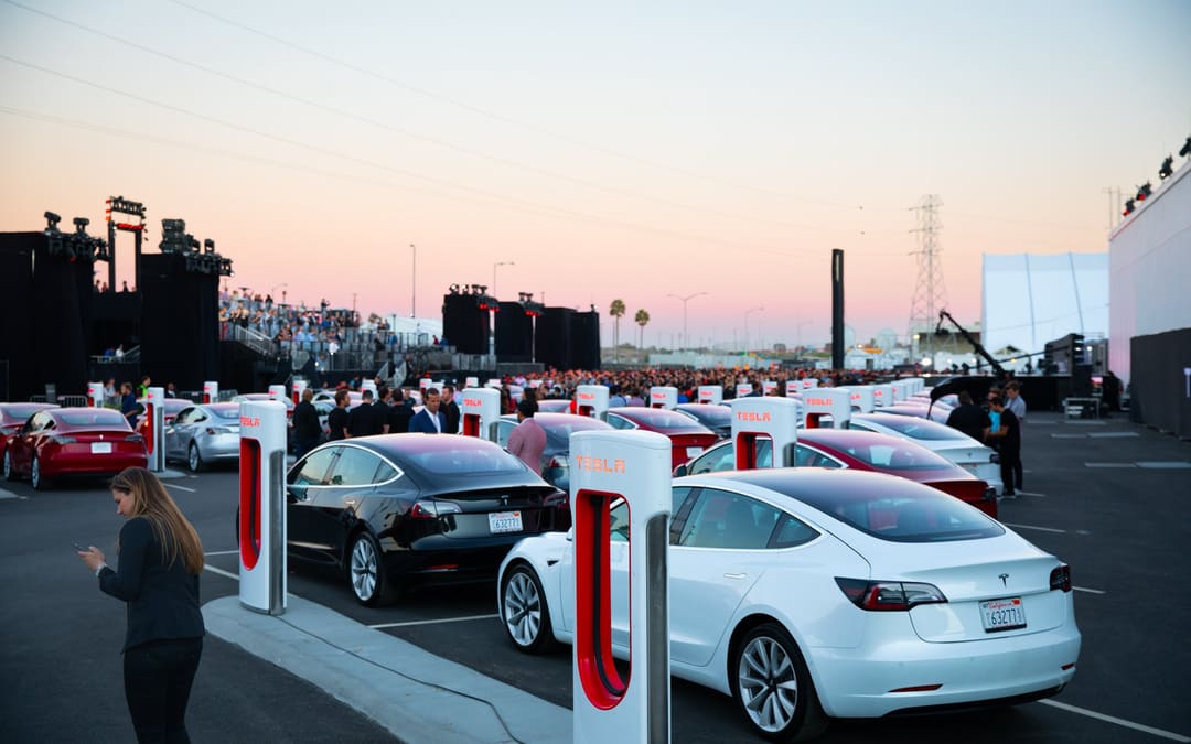 Model 3 cars charging at a Tesla Supercharger station at dusk, from Tesla’s “10 years of Model 3” post