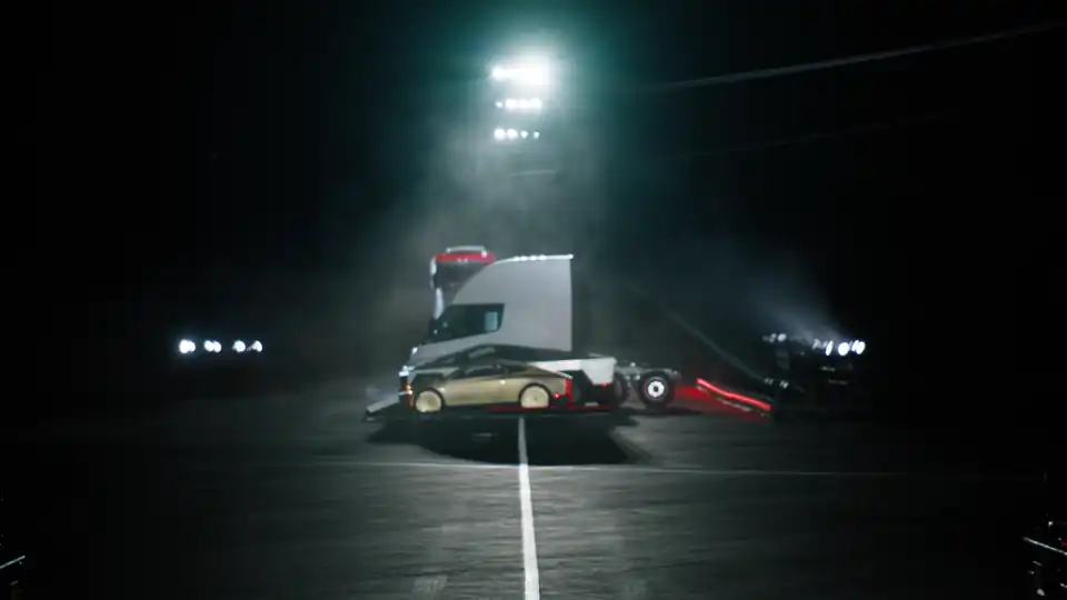 Tesla Roadster upside down in the air above a lineup of Tesla vehicles at night, thrusters firing, from Tesla's official kickflip video