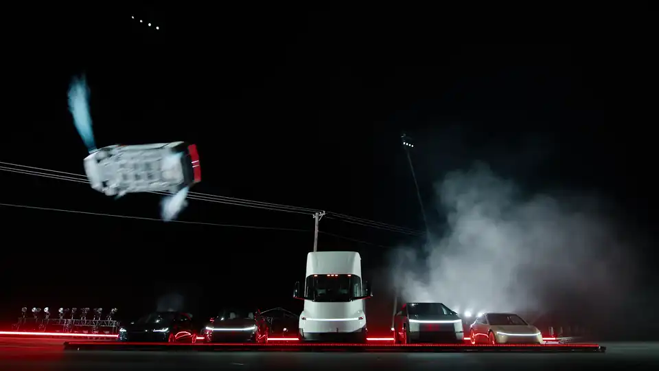 Tesla Roadster upside down above a lineup of Tesla vehicles at night, from Tesla's official kickflip video